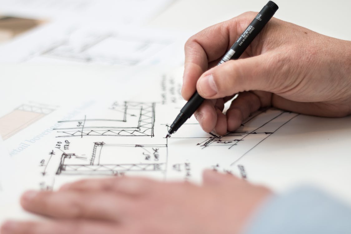 Free Close-up of hand drawing intricate technical designs on blueprint with pen, ideal for engineering or architecture themes. Stock Photo